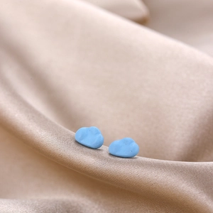 Macro shot of 3D light blue cloud stud earrings on elegant silk satin fabric texture