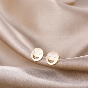 Close-up of Y2K gold smile face stud earrings with white heart eyes on silk fabric