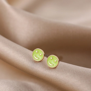 Macro shot of green enamel smiley face earrings on champagne silk background