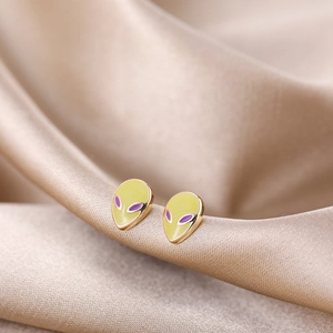 Close-up of golden alien stud earrings with yellow enamel on champagne silk background