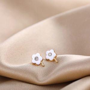 Macro shot of white enamel daisy earrings with gold edges and central zircon stone