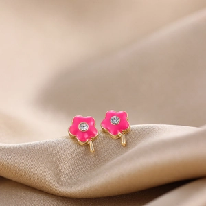 Macro detail of pink flower stud earrings with gold base and zircon center on satin