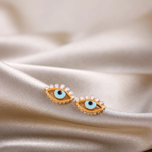 Detail of evil eye stud earring with orange enamel and gold base on silk background