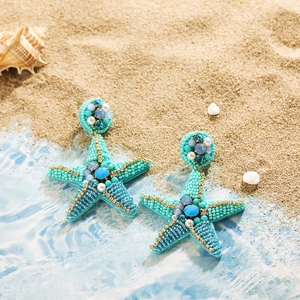 Détail de boucles d'oreilles étoile de mer bleues en perles sur fond de plage sableuse