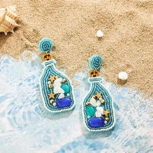 Vue détaillée des boucles d'oreilles bouteille avec perles sur fond de sable marin