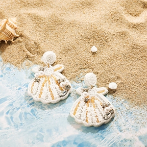 Détail de boucles d'oreilles coquillage avec perles blanches et strass sur sable
