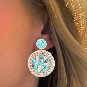 Détail de boucles d'oreilles en perles bleues avec coquillages et texture de paille