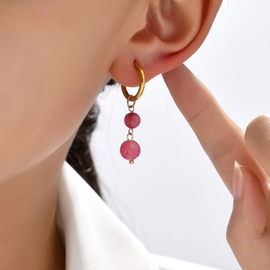 Asymmetric gold hoop earrings with double pink natural stone beads on a model
