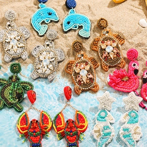 Vue détaillée de boucles d'oreilles en perles animaux marins sur plage de sable