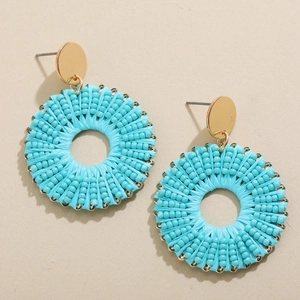 Détail de boucles d'oreilles créoles en perles bleues avec clous dorés sur fond beige