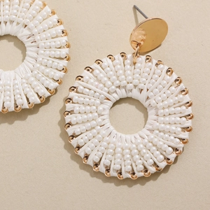Détail de boucles d'oreilles bohèmes avec fibre tressée blanche et perles dorées fines