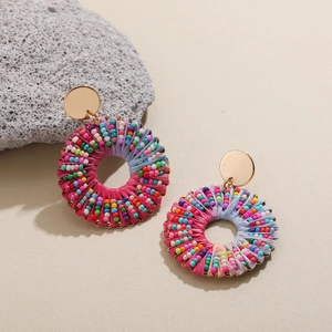 Détail de boucles d'oreilles bohèmes en raphia avec perles colorées et clous en métal doré