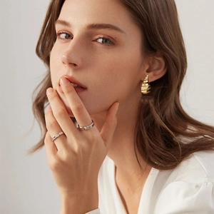 Detalle de una modelo con pendientes de gota en espiral y anillos de diamantes
