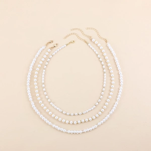 Détail de trois colliers de perles blanches superposés avec perles dorées et cristal