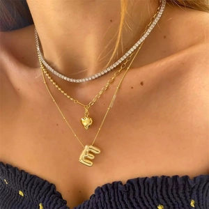 Detail van gelaagde 18K gouden kettingen met ballonletter E en hartvormige hanger