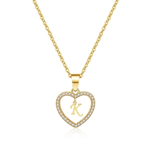 Macro shot of gold heart necklace with zircon inlay and letter K pendant on white background