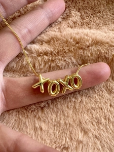 Detailed view of hand-held gold XOXO pendant necklace with high-polished metal finish