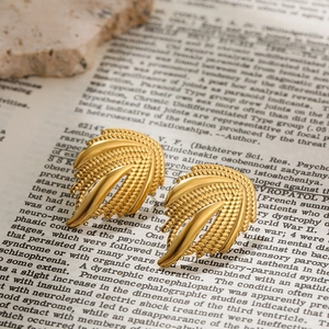 Détail de boucles d'oreilles dorées en forme d'ailes avec texture fine sur page vintage