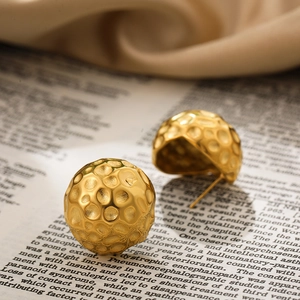 Détail de boucles d'oreilles boules dorées avec texture martelée sur papier vintage