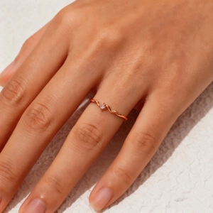 Close-up of a minimalist rose gold wave ring featuring a single zircon on a finger