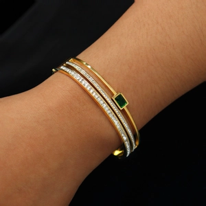 Detail of layered gold bracelet featuring a rectangular emerald and pavé-set crystals