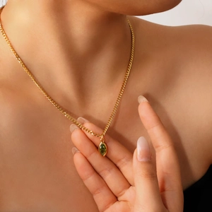 Close-up of a gold flat chain necklace with a marquise olive green gemstone on the neck