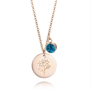 Détail du collier en or rose avec disque gravé de fleurs et pendentif en zircon bleu