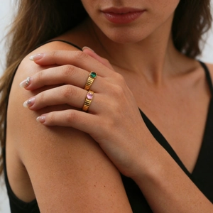 Primo piano di anelli d'oro a coste con pietre preziose verde smeraldo e rosa sulla mano