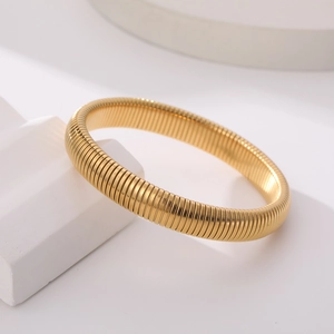 Detail van een flexibele 18K vergulde gaspipe armband op witte geometrische props