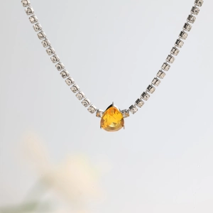 Detail of silver tennis necklace with square zircons and a pear-cut yellow gemstone pendant