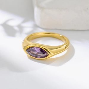 Bague élégante en titane doré avec une pierre violette marquise sur une surface en pierre