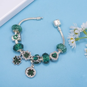 Pandora style snake chain bracelet with green crystal beads and clover charms on blue background