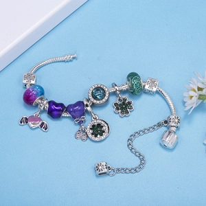 Silbernes Schlangen-Armband mit violetten Charms und Kleeblatt-Anhänger auf blauem Grund