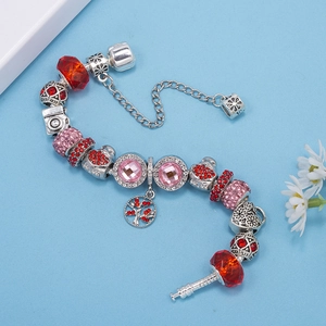 Detalle de pulsera de dijes con colgante de cámara y corazón de cristal rojo