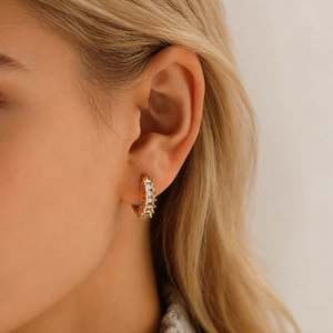 Close-up of gold hoop earrings with vertical baguette-cut zircons worn by a model