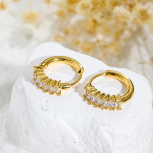 Minimalist gold hoop earrings with rectangular zircons on a white textured stone