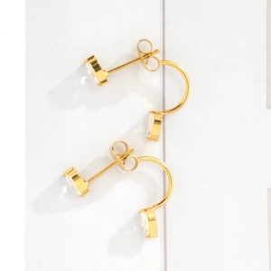 Close-up of golden C-shaped stud earrings with sparkling rectangular zircon stones