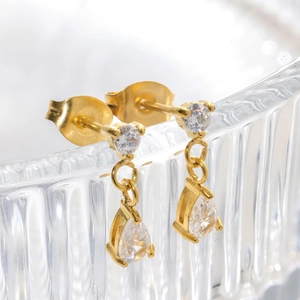 Detail of gold teardrop earrings with clear cubic zirconia hanging on glass
