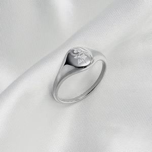 Close-up of a silver signet ring with sun and flower engravings on a white satin cloth