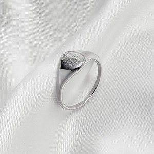 Macro shot of silver signet ring with engraved flower pattern on white silk