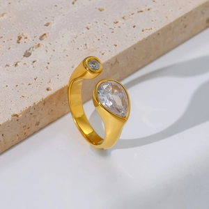 Close-up of gold open ring with pear and round shaped zircon stones on stone background
