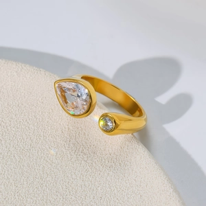 Detailed view of a gold open ring featuring a pear-cut and round crystal on a stand