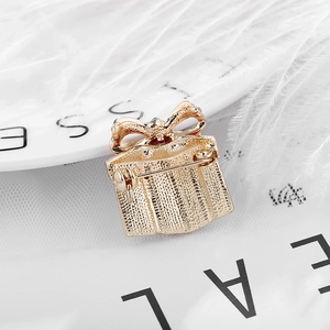 Golden gift box brooch with bow and back pin details on white feather background