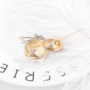 Back view of gold snowman brooch with pin clasp on decorative white plate with feathers