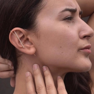 Close-up of a minimalist gold lightning cartilage piercing with inlaid pearls and zircons
