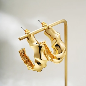 Detailed view of thick gold twisted C-shape earrings on a minimalist metal display stand