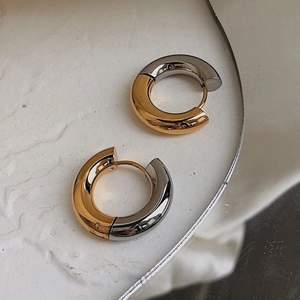 Macro view of minimalist 18K gold and silver two-tone hoop earrings on stone tray