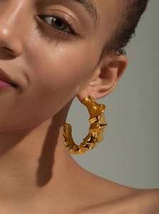 Macro detail of gold C-shape hoop earrings featuring a unique molten lava texture
