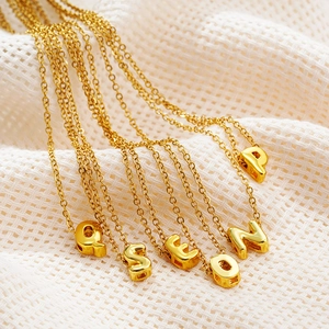 Macro detail of polished gold bubble alphabet pendants on fine stainless steel chains
