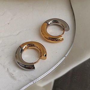 Macro shot of two-tone gold and silver stainless steel hoop earrings on a stone surface